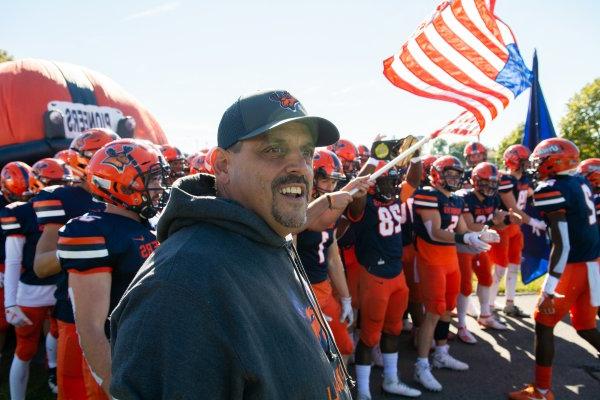 Coach Blaise Faggiano stands ahead of football players waving Pioneers flag