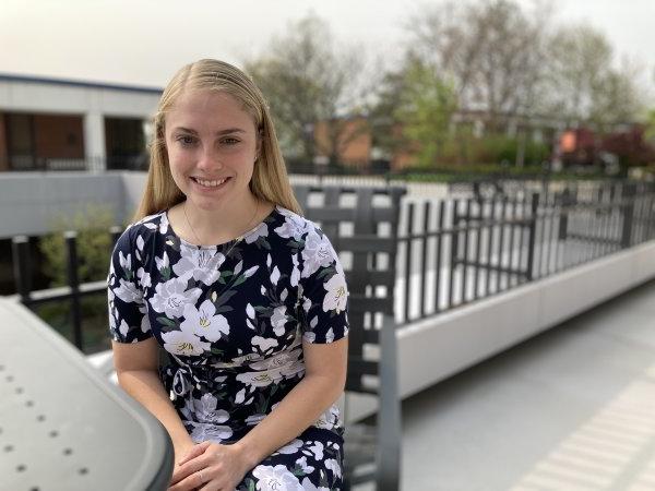 Isabelle LaBelle '23, in floral dress, sits at a table in the courtyard outside the library.